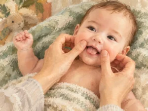 Gemalte Szene: Zwei Hände streichen sanft über die Wangen eines lachenden Babys.