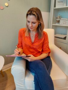 Carina Welzel sitzt in einem hellen Sessel und schreibt sich Notizen auf.